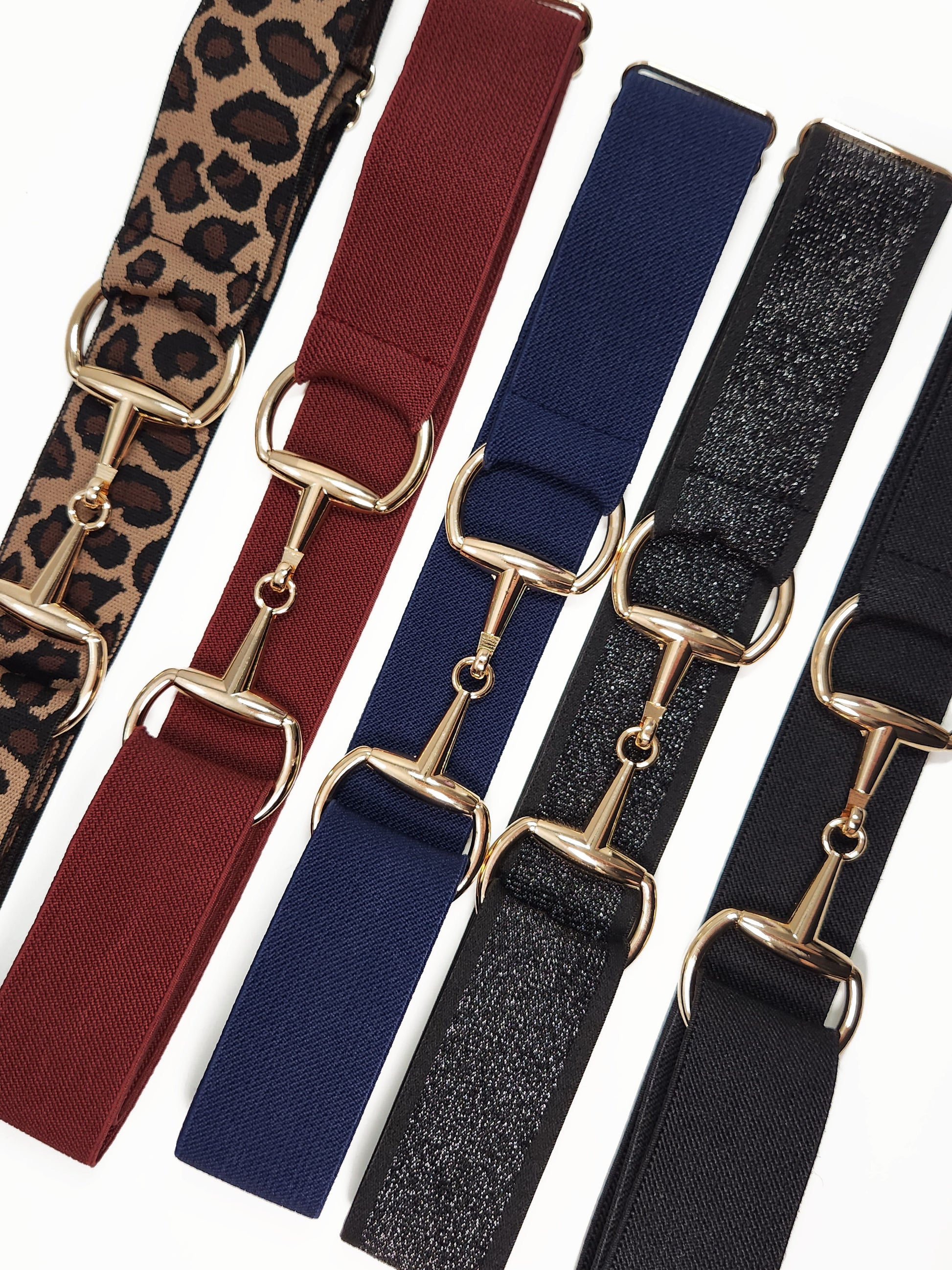 Assorted bit belts with gold buckles in multiple colors and prints for equestrian use.

